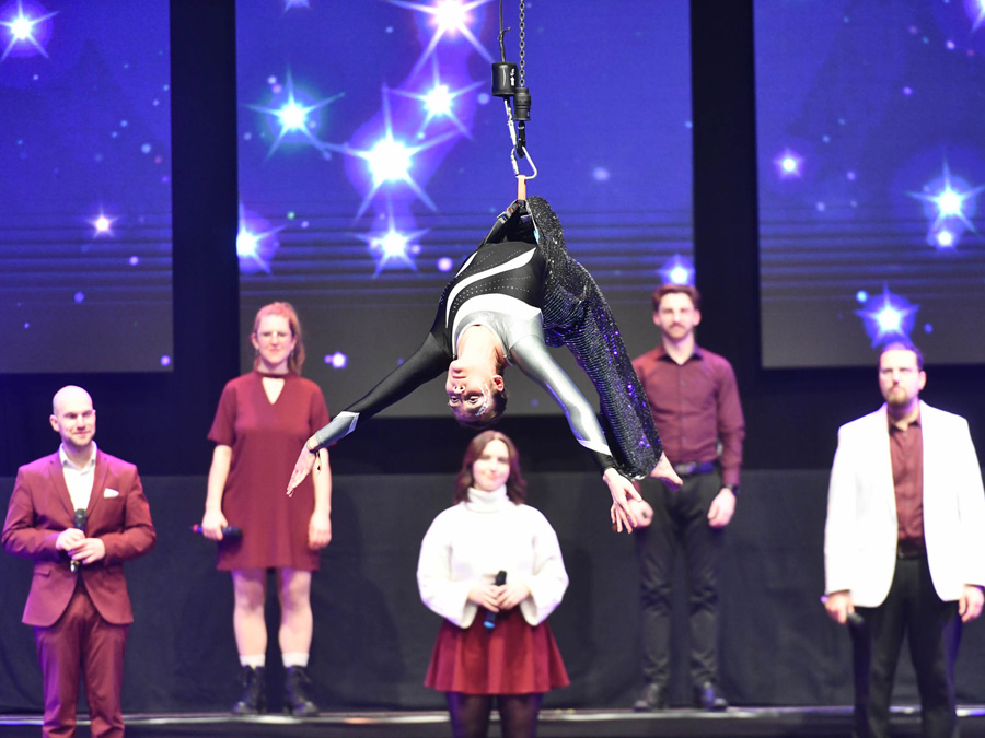 Schwebender Moment in der Arena: Eine Akrobatin der Akrobatikgruppe des SV Fortuna Regensburg seilt sich kontrolliert aus großer Höhe ab und landet sicher auf der Bühne