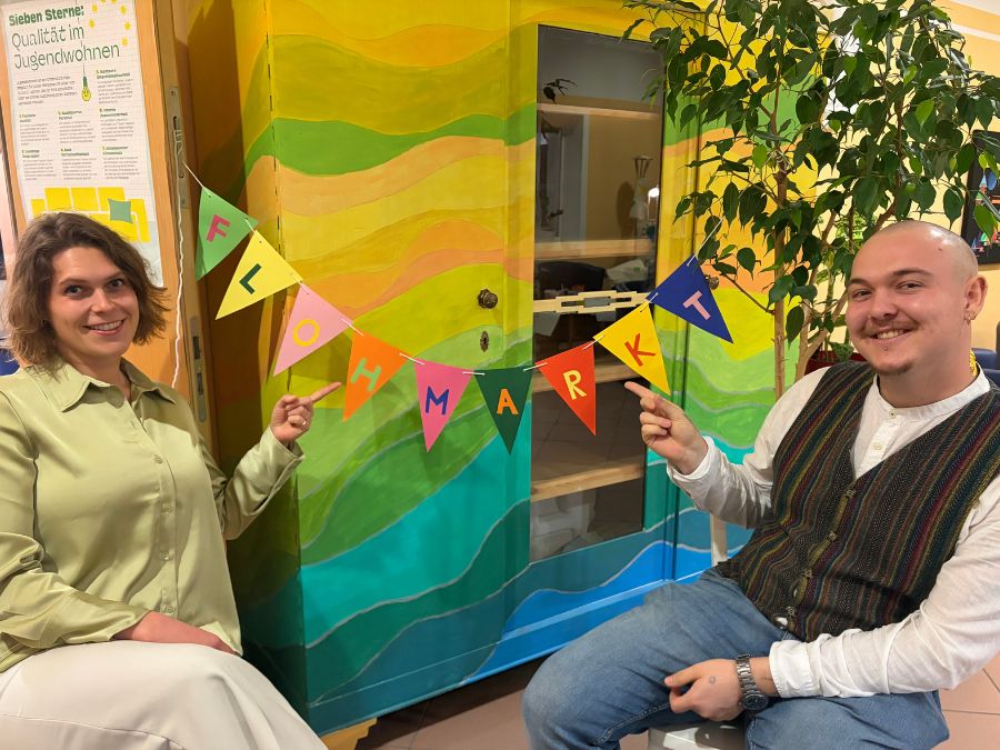 Die Organisatoren der Nacht der Nachhaltigkeit deuten auf ein Banner mit dem Wort Flohmarkt.