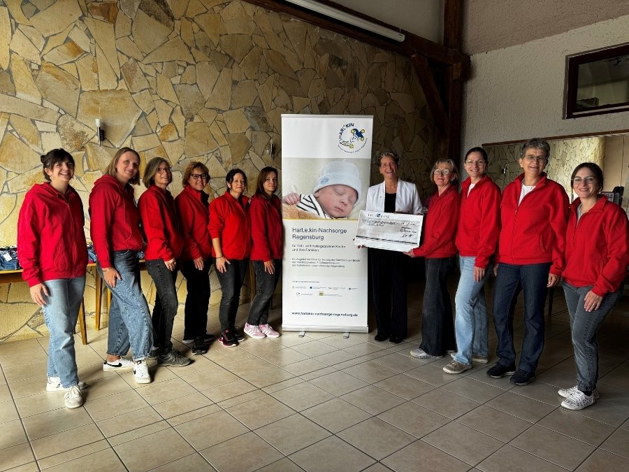 Petra Weickert (4te von rechts) übergibt mit dem Team des Kinderbasars den Spendenscheck für Harl.e.kin an KJF-Abteilungsleiterin Chiara Thoma (5te von rechts). (Foto: Sophia Lorenz)